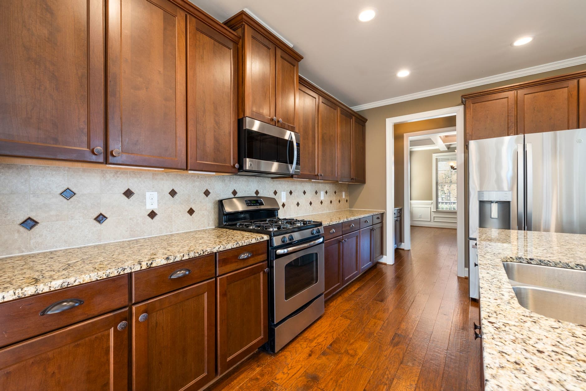 Wood kitchen cabinets, granite counters, tile backsplash, and stainless appliances, the SKU-dense room a kitchen and bath spec has to lock